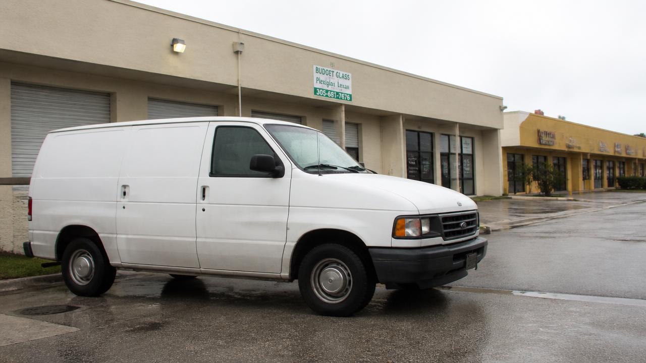 A plain white service van parked on a wet South Florida street